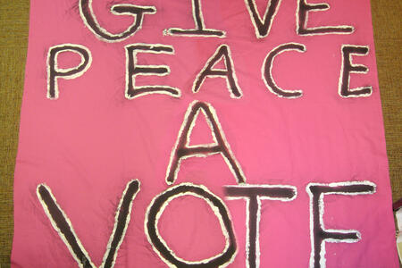 Pink poster with black text with a white outline reading "Give Peace a Vote"