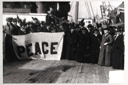 Black and white photograph of a crowd of people on a dock holding a large banner saying "PEACE"